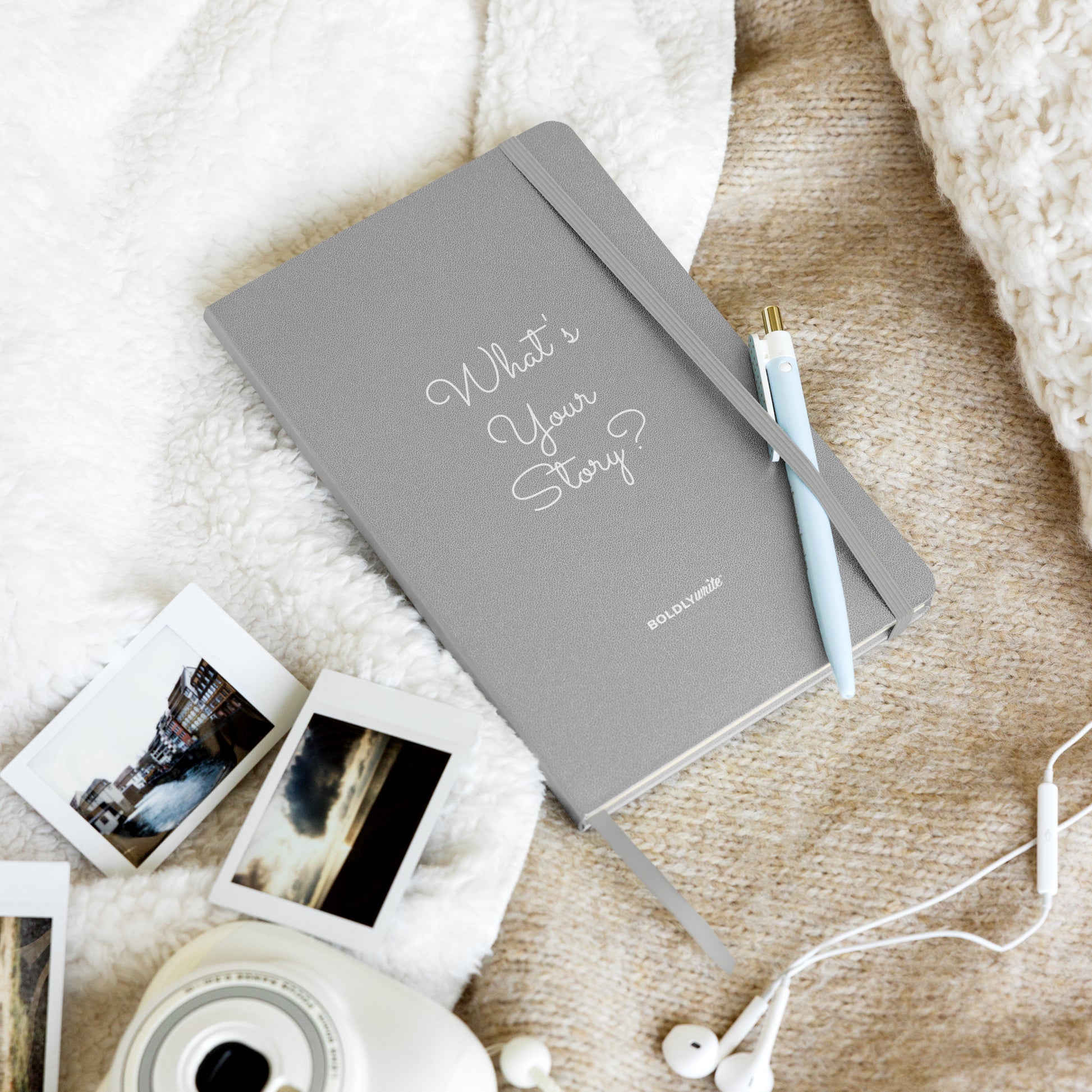 What's Your Story? grey hardcover journal with pen, Polaroid photos, and earphones on a cozy cream blanket – Boldly Write